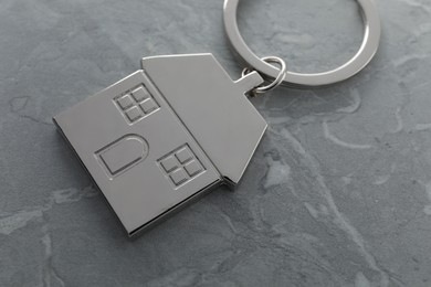 Metal keychain in shape of house on grey marble table, closeup