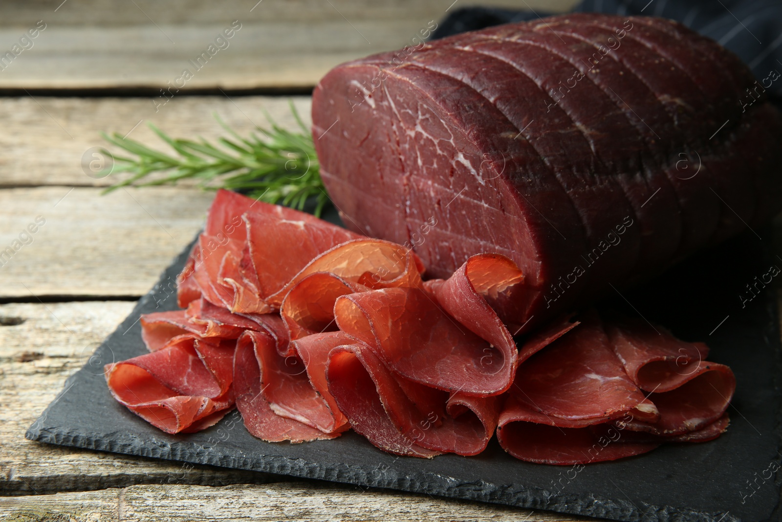 Photo of Tasty bresaola and rosemary on wooden table, closeup