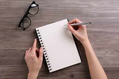 Photo of Woman writing in notebook at wooden table, top view