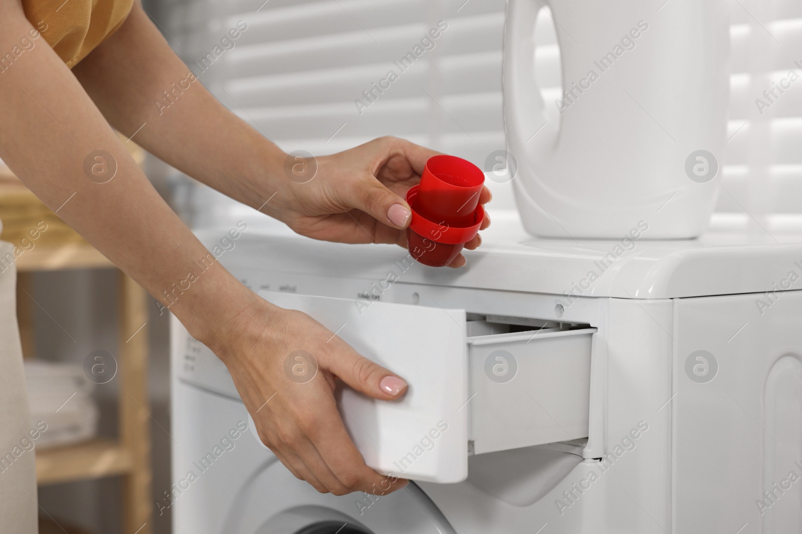 Photo of Woman with laundry detergent near washing machine indoors, closeup