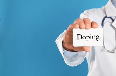 Image of Doctor holding card with word Doping on light blue background, closeup. Space for text