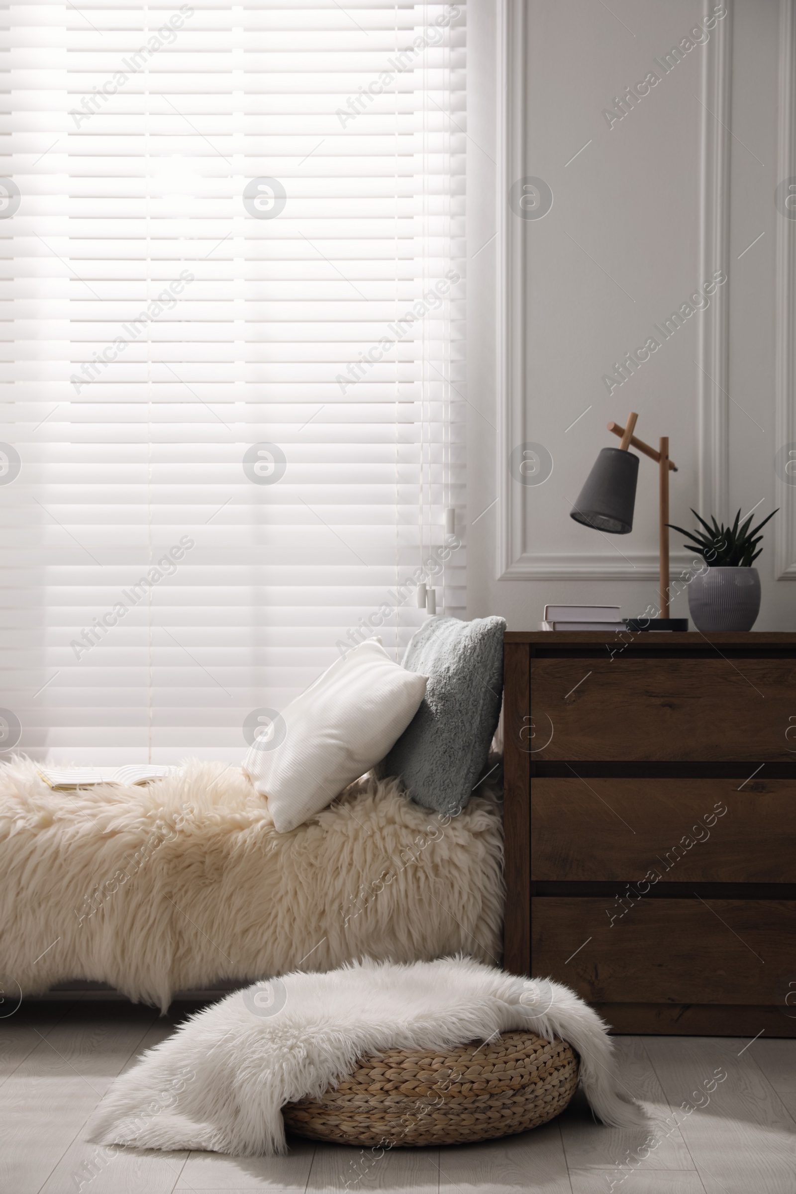 Photo of Comfortable place for relax with faux fur and pillows near window in room