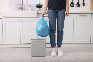 Photo of Woman taking garbage bag out of trash bin in kitchen, closeup