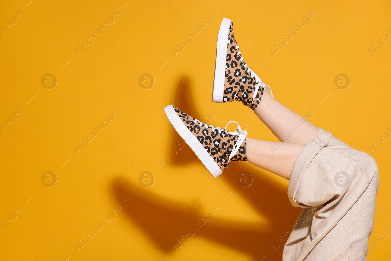 Photo of Woman posing in classic old school sneakers with leopard print on orange background, closeup. Space for text