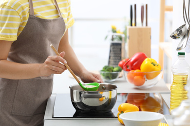 Young woman cooking tasty soup in kitchen, closeup