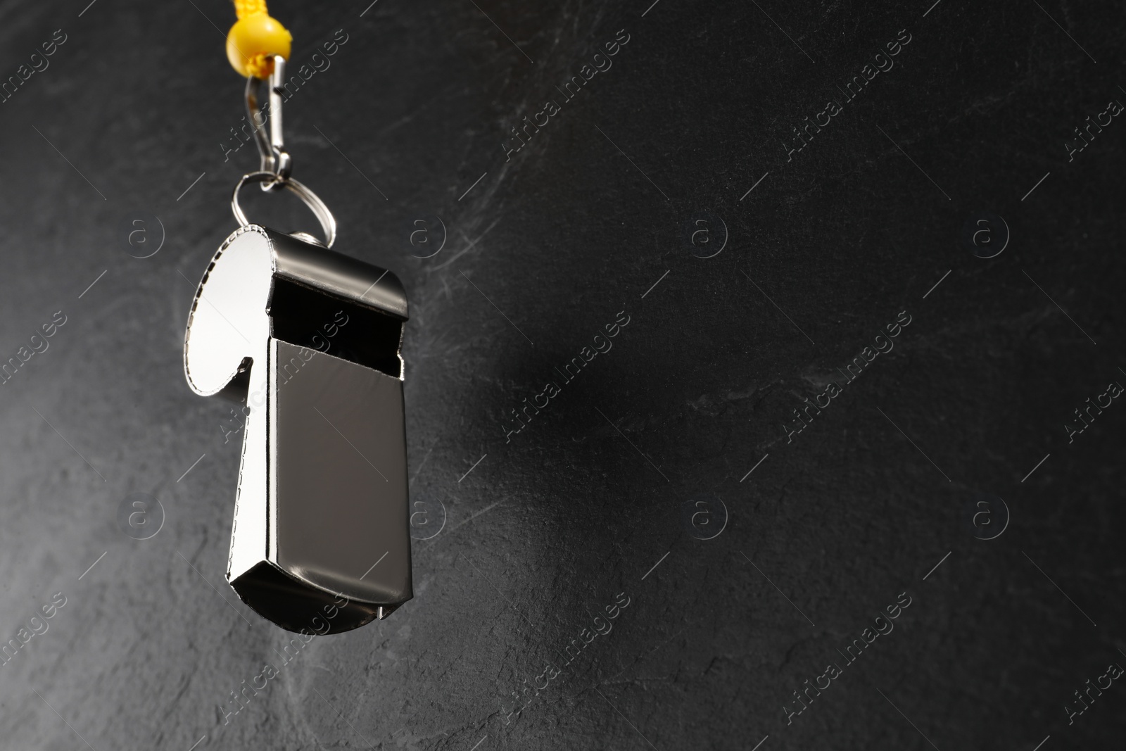 Photo of Referee equipment. Metal whistle on black textured background, closeup and space for text