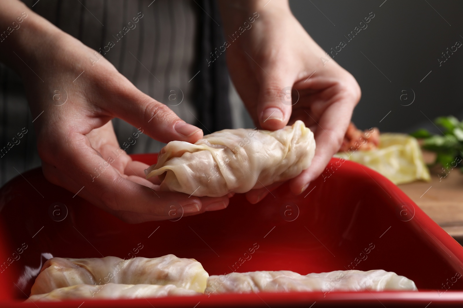 Photo of Woman putting uncooked stuffed cabbage roll into baking dish at table, closeup