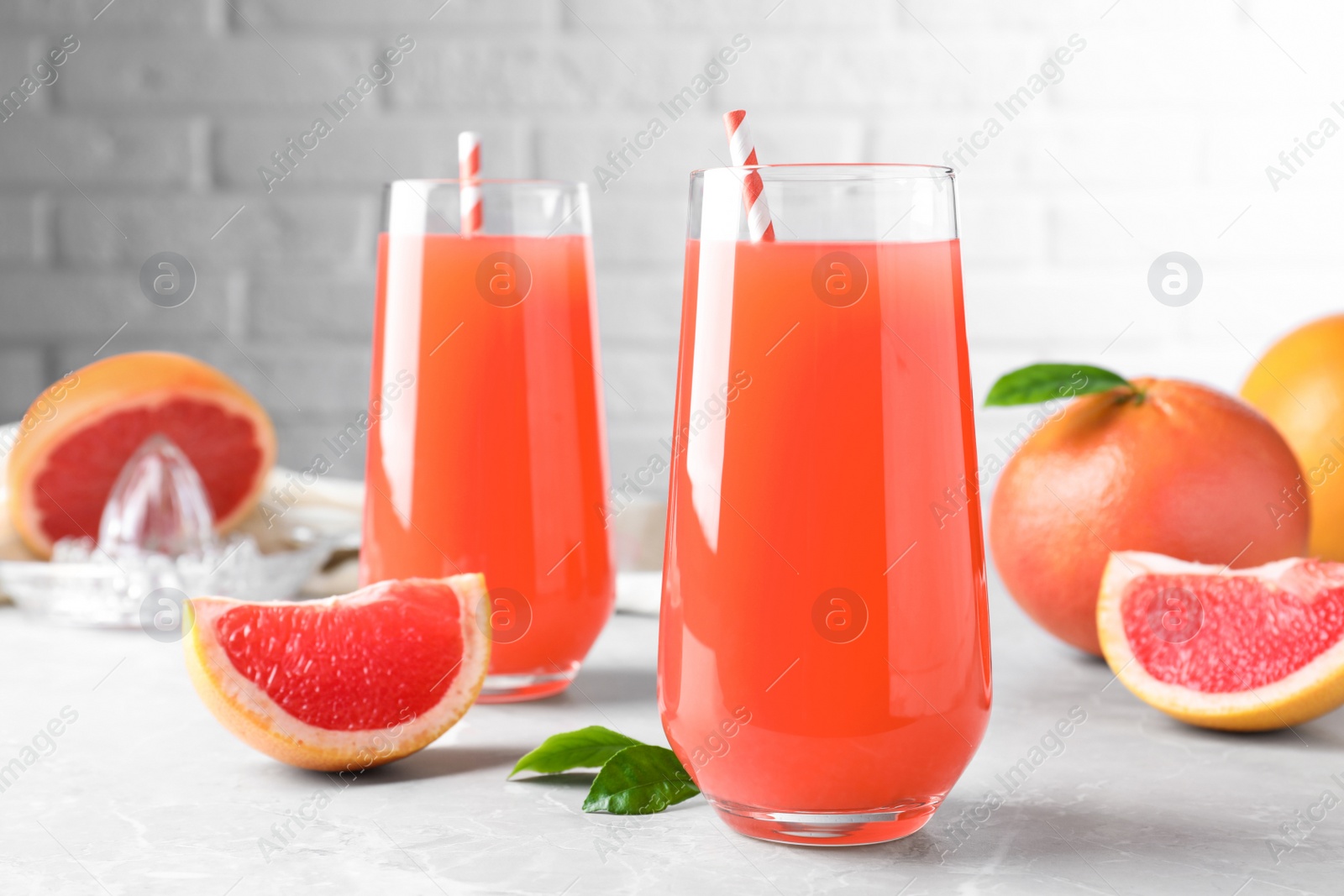 Photo of Tasty freshly made grapefruit juice and fruit on light grey marble table