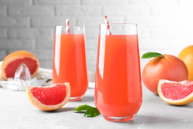 Tasty freshly made grapefruit juice and fruit on light grey marble table