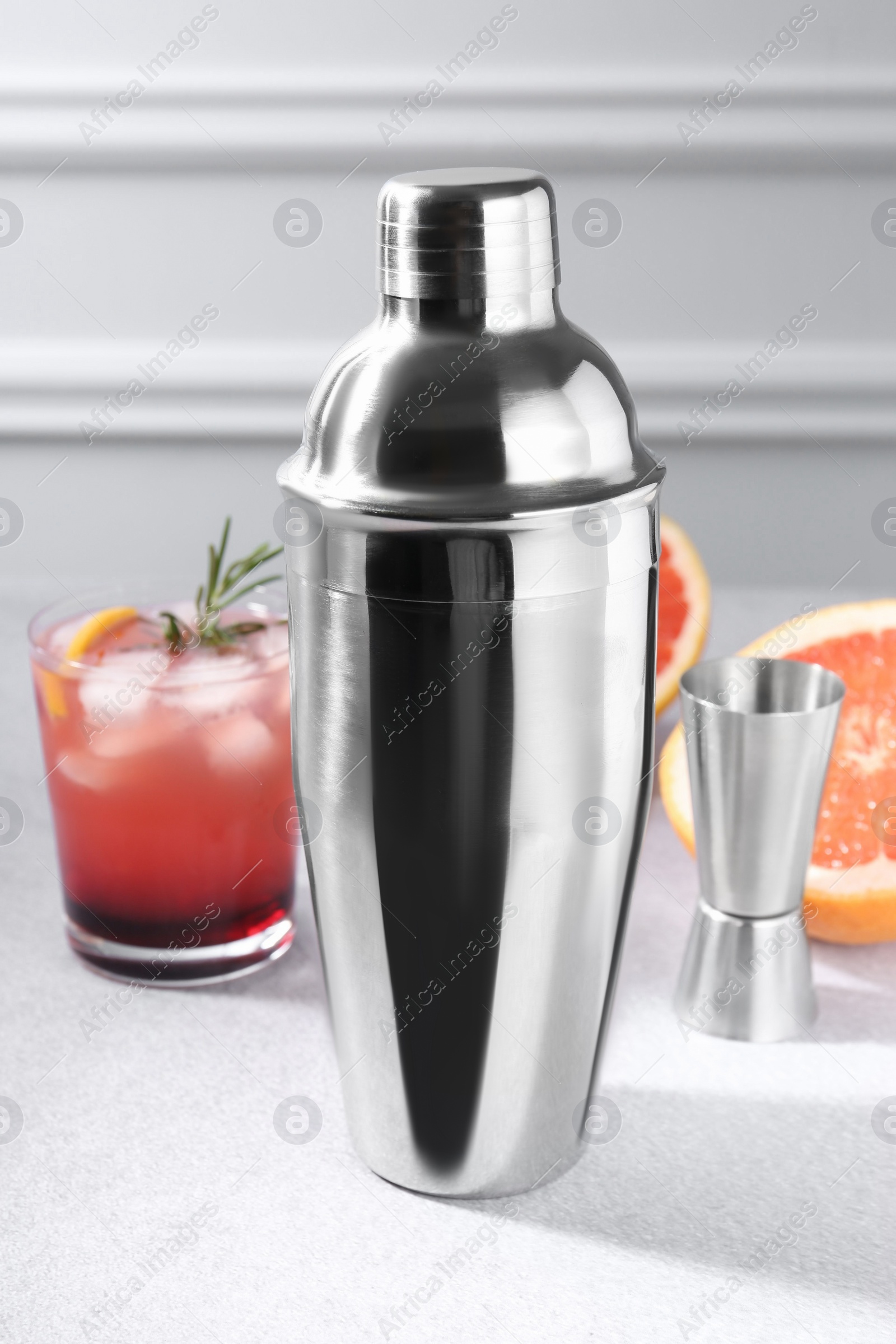 Photo of Metal shaker, delicious cocktail, jigger and grapefruit on light grey table