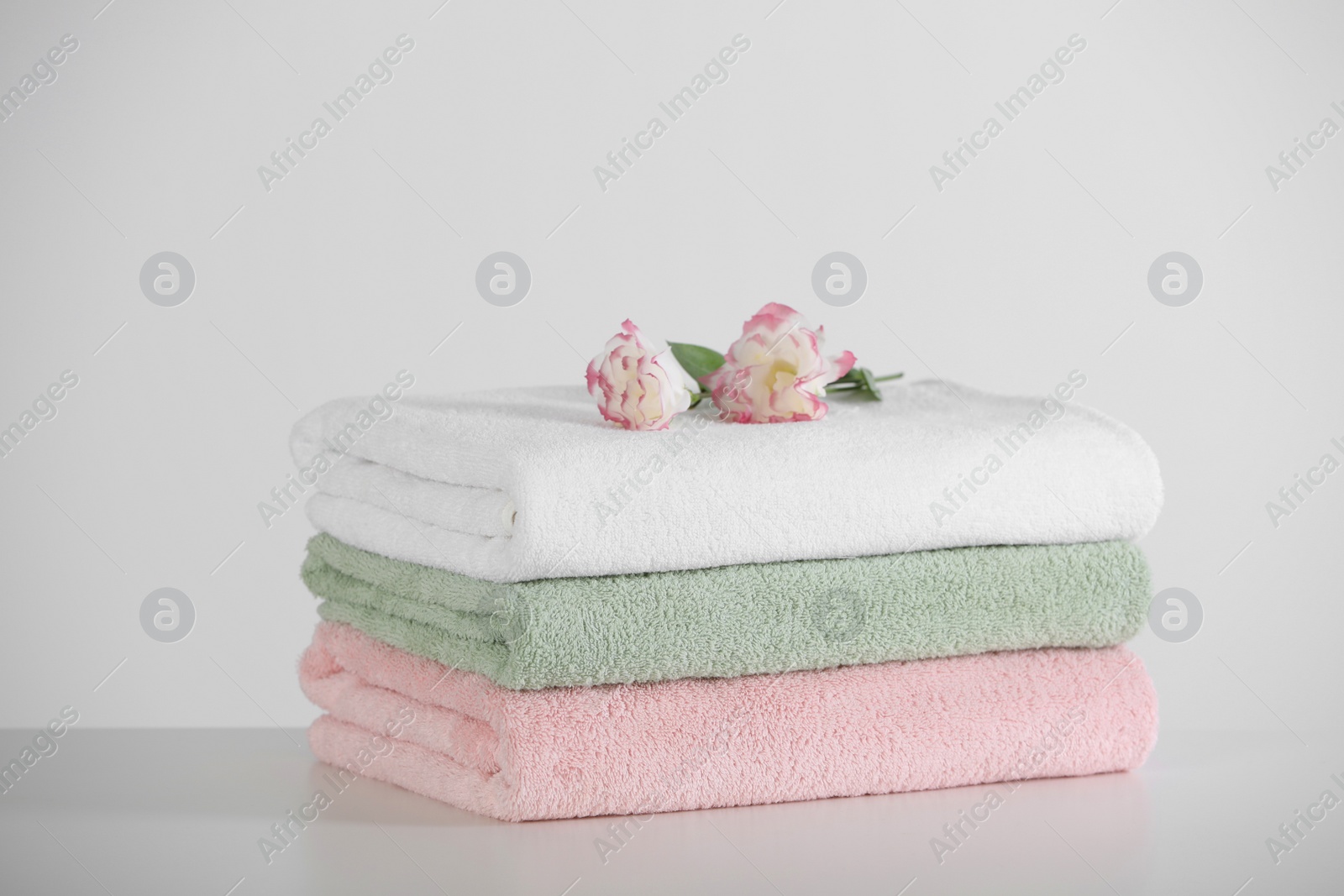 Photo of Soft folded towels with eustoma flowers on white table