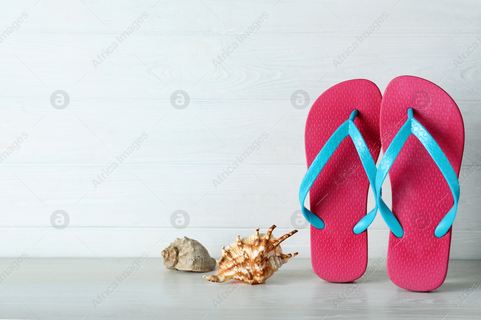 Photo of Stylish flip flops and seashells near white wooden wall, space for text