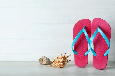 Photo of Stylish flip flops and seashells near white wooden wall, space for text