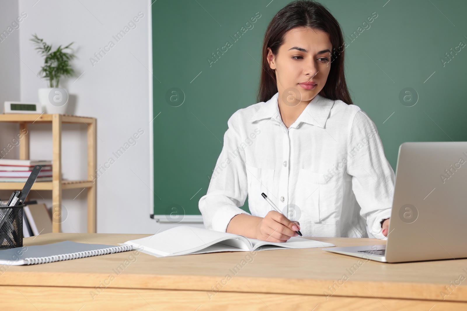 Photo of Young teacher giving lesson at table in classroom