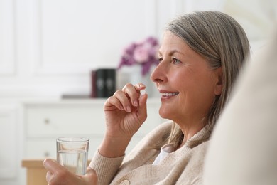 Photo of Beautiful senior woman with glass of water taking pill at home