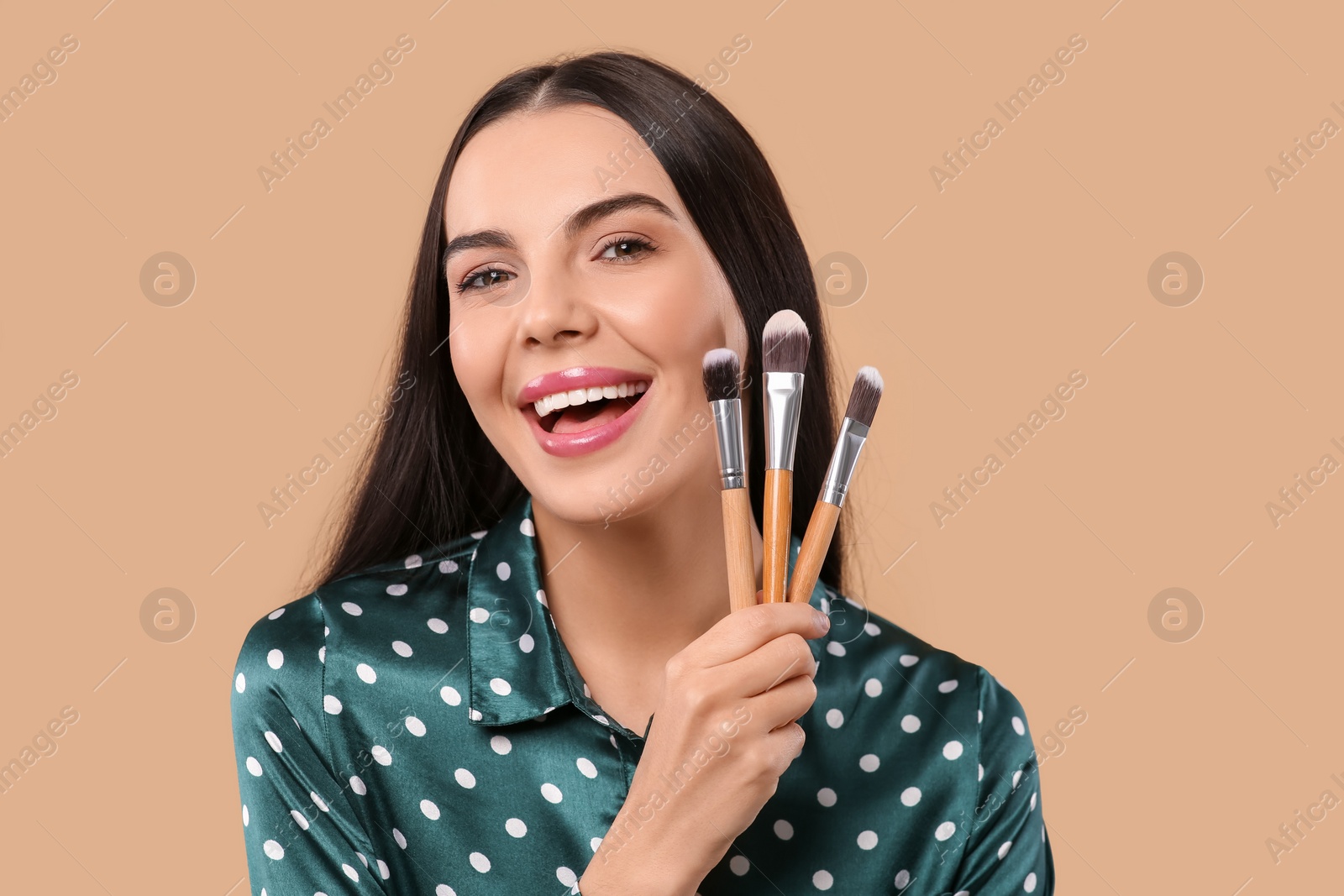 Photo of Happy woman with different makeup brushes on light brown background