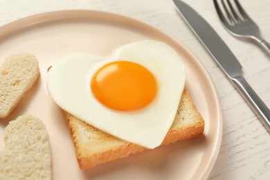 Plate with heart shaped fried egg served on white wooden table, closeup