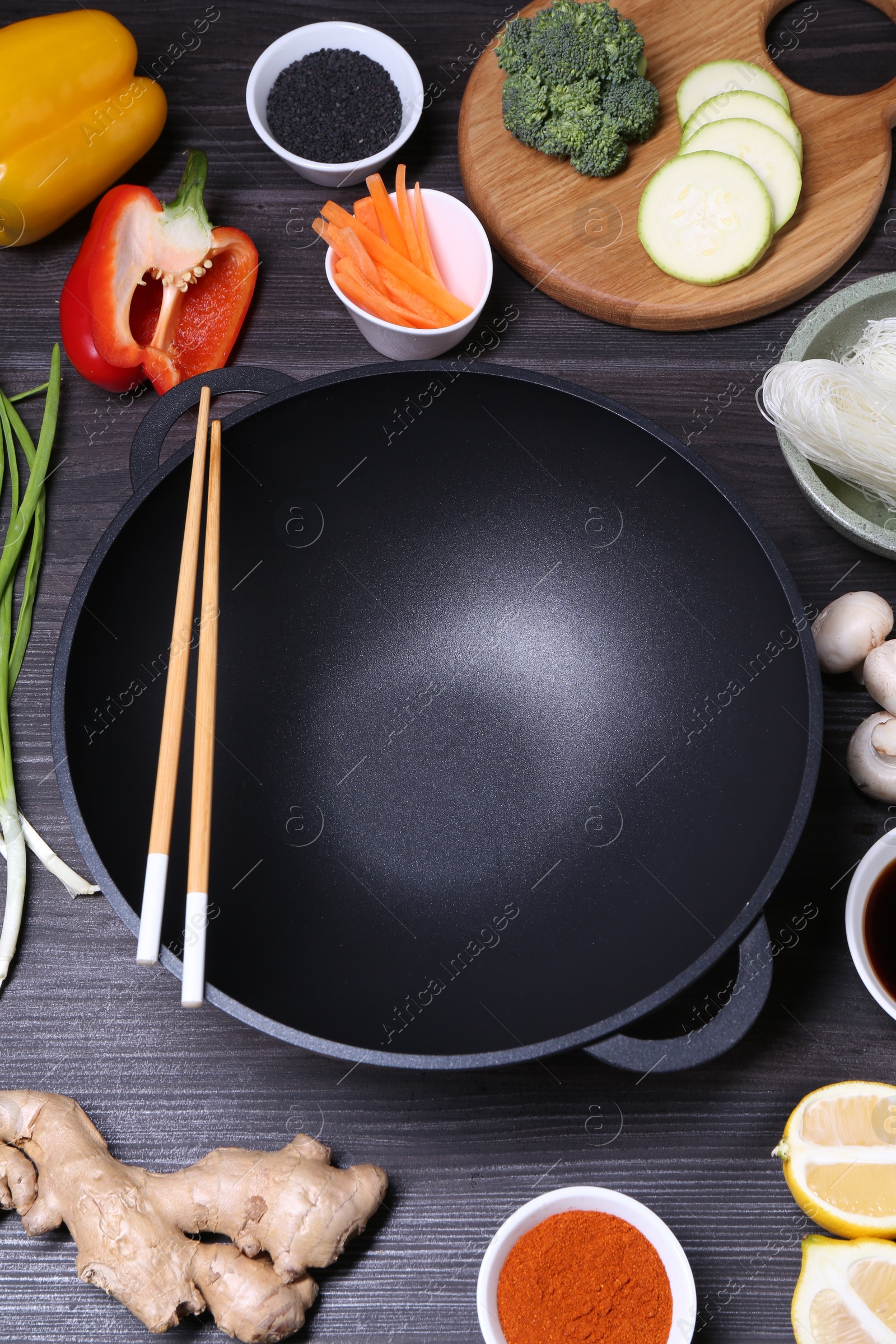 Photo of Empty iron wok, chopsticks and ingredients on dark grey wooden table, above view