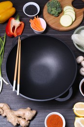 Photo of Empty iron wok, chopsticks and ingredients on dark grey wooden table, above view