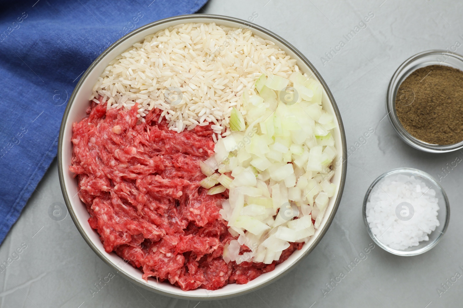 Photo of Bowl of forcemeat, chopped onion with rice and spices for preparing stuffed cabbage rolls on light grey table, flat lay