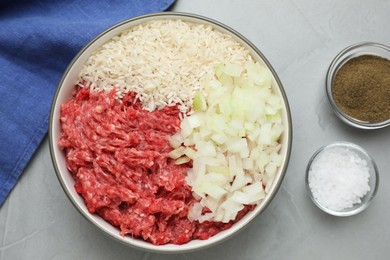 Bowl of forcemeat, chopped onion with rice and spices for preparing stuffed cabbage rolls on light grey table, flat lay