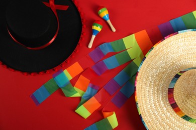 Photo of Mexican sombrero and black Flamenco hats and maracas on red background, flat lay
