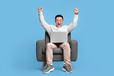 Photo of Emotional man with laptop sitting in armchair on light blue background