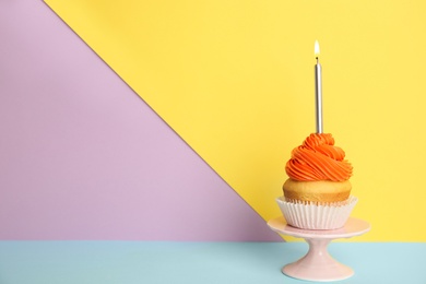 Photo of Birthday cupcake with candle on stand against color background, space for text