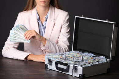 Photo of Businesswoman with case of dollar bills at wooden table, closeup