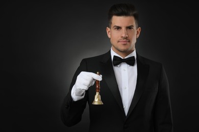 Photo of Butler holding hand bell on black background, space for text