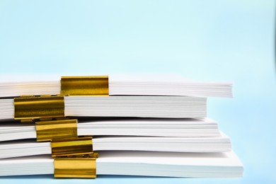 Photo of Many sheets of paper with golden clips on light blue background, closeup