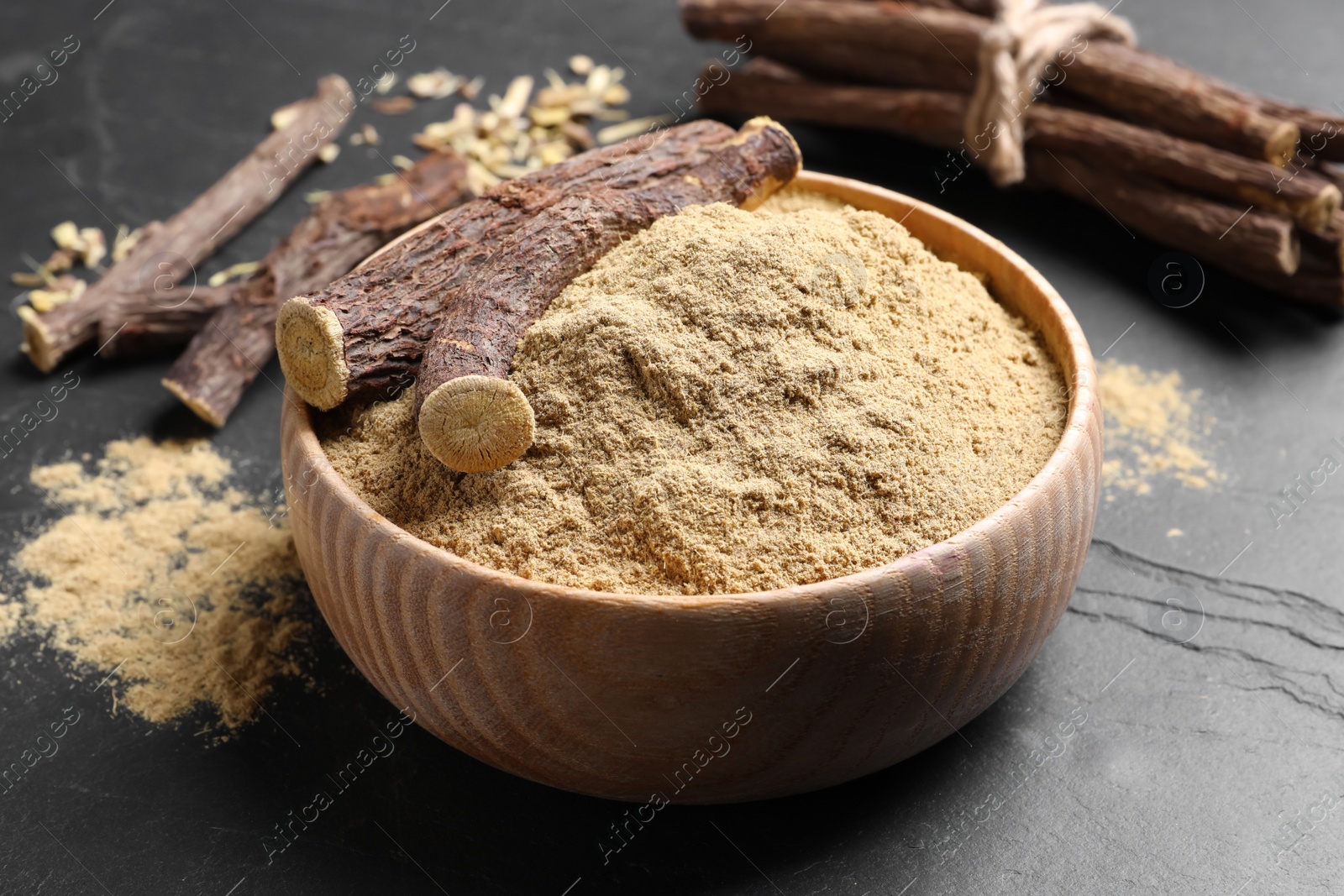Photo of Powder in bowl and dried sticks of liquorice root on black table