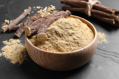 Powder in bowl and dried sticks of liquorice root on black table