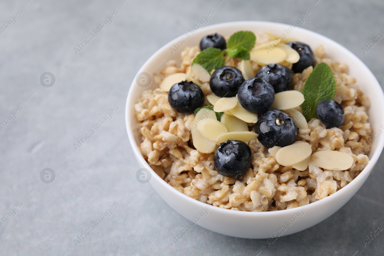 Photo of Tasty oatmeal with blueberries, mint and almond petals in bowl on grey table. Space for text