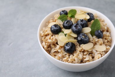 Photo of Tasty oatmeal with blueberries, mint and almond petals in bowl on grey table. Space for text