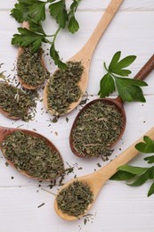 Photo of Spoons with dried aromatic parsley and fresh leaves on white wooden table, flat lay