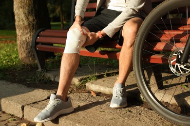 Photo of Man with injured knee on bench near bicycle outdoors, closeup