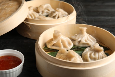 Bamboo steamers with tasty baozi dumplings and bowl of sauce on table