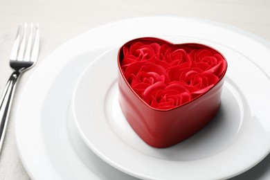 Photo of Decorative heart shaped box with roses on white dishware for romantic dinner on white table, closeup