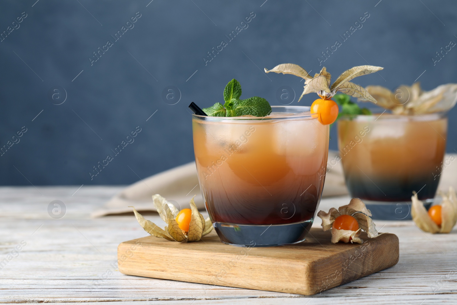 Photo of Refreshing cocktail decorated with physalis fruit on wooden table against grey background. Space for text