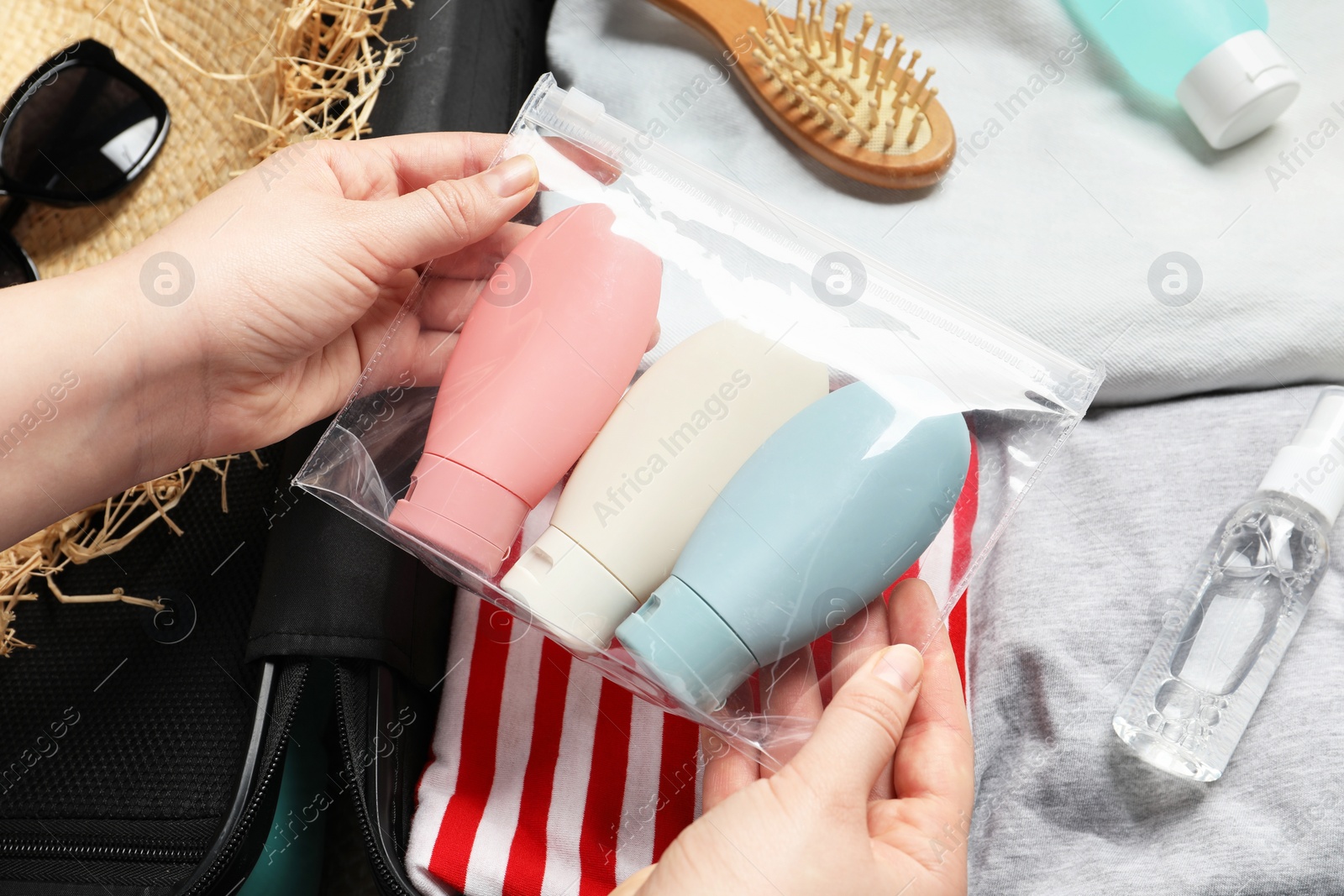 Photo of Woman with plastic bag of cosmetic travel kit packing suitcase, top view