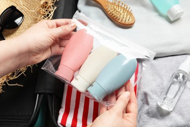 Photo of Woman with plastic bag of cosmetic travel kit packing suitcase, top view