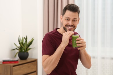 Photo of Happy man drinking delicious fresh smoothie at home