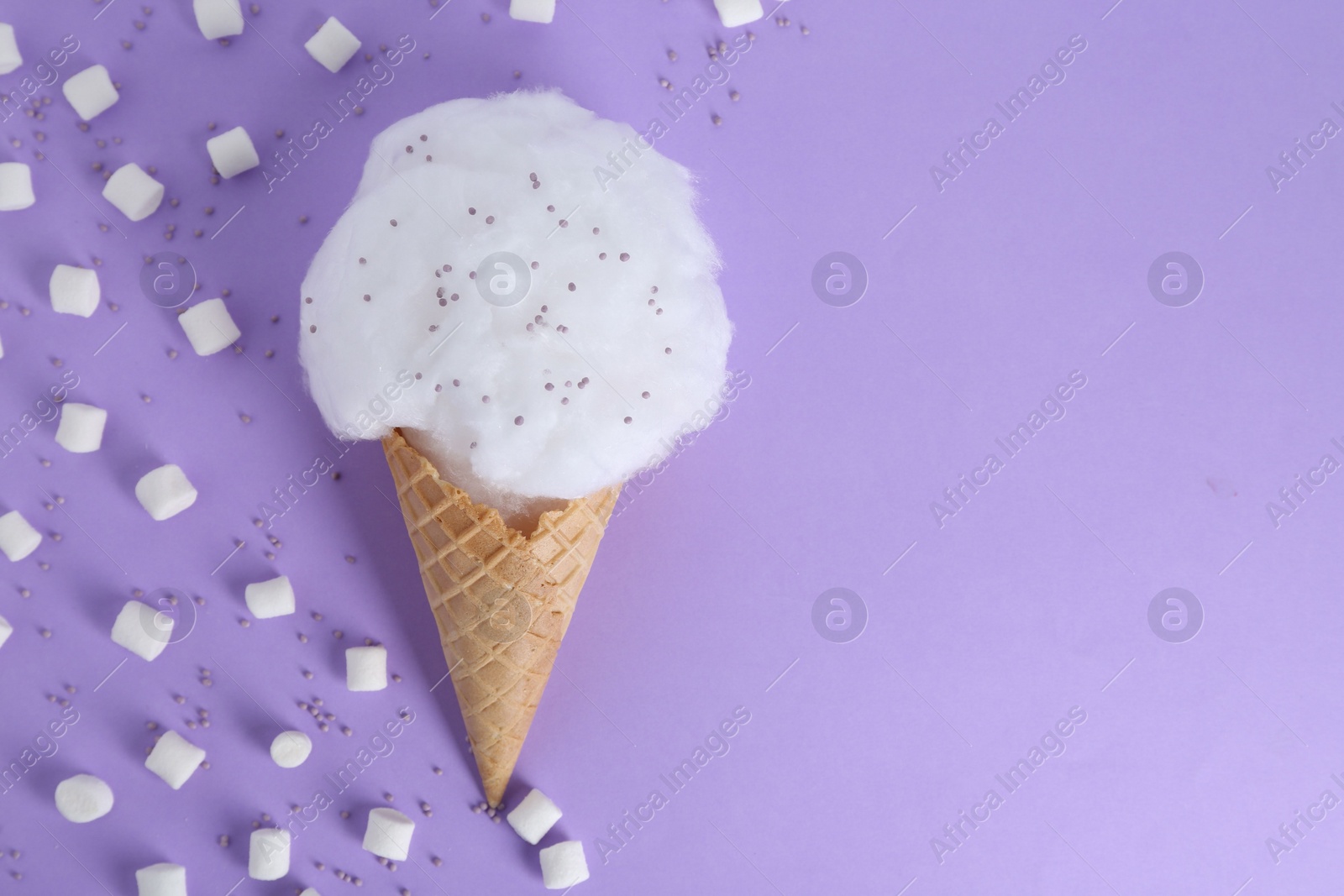 Photo of Sweet cotton candy in waffle cone and marshmallows on purple background, flat lay. Space for text