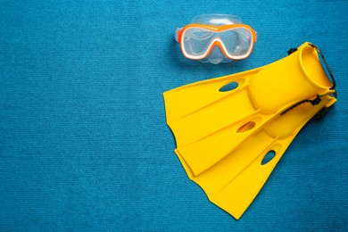 Photo of Pair of yellow flippers and mask on blue fabric, flat lay. Space for text