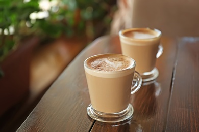 Photo of Cups of aromatic coffee with foam on wooden table