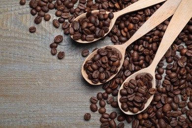 Spoons with roasted coffee beans on wooden table, flat lay. Space for text