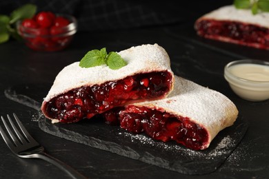 Photo of Delicious strudel with cherries, powdered sugar and mint on black table