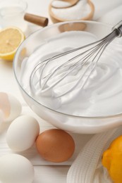 Photo of Bowl with whipped cream, whisk and ingredients on white wooden table, closeup