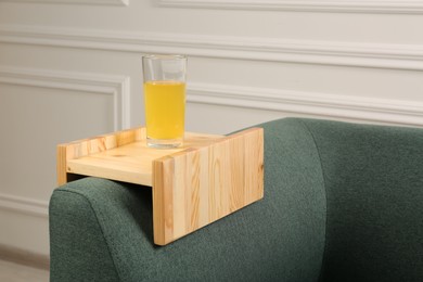 Photo of Glass of juice on sofa with wooden armrest table in room. Interior element